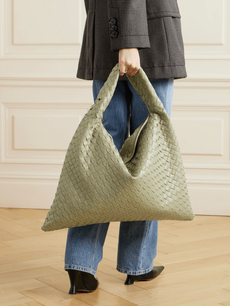 Woman carrying a large sage green woven leather Bottega Veneta bag with jeans and a blazer